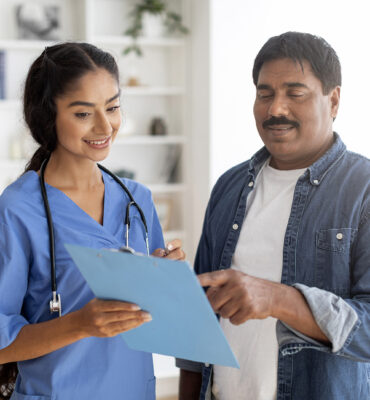 Young Indian Doctor Lady Discussing Medical Treatment With Male Patient In Clinic Young Indian Doctor Lady Discussing Medical Treatment With Male Patient During Meeting In Clinic Office, Friendly Therapist Woman Holding Clipboard, Showing Prescription Details To Smiling Man